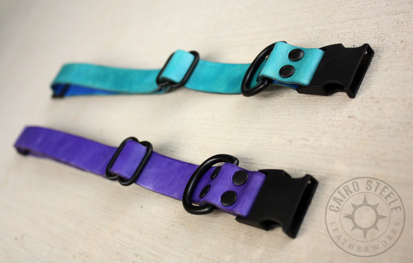 The two collars, unbuckled and laid flat, viewed at an angle from the end with the D-ring