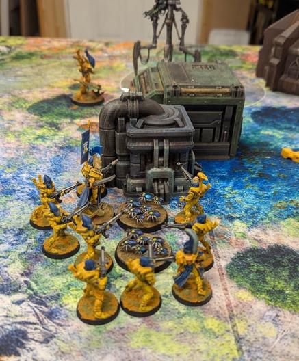 A miniature wargame in progress. A group of space elf warriors surround some robot scarabs.