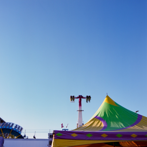Another ride rises up behind some tents towards a clear blue sky.