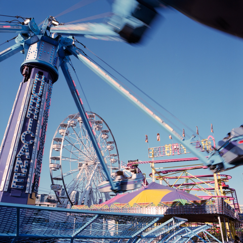 A chaotic view through The Hurricane in full spin and the pink and yellow tracks of the Crazy Mouse to the teacup and saucer ferris wheel.