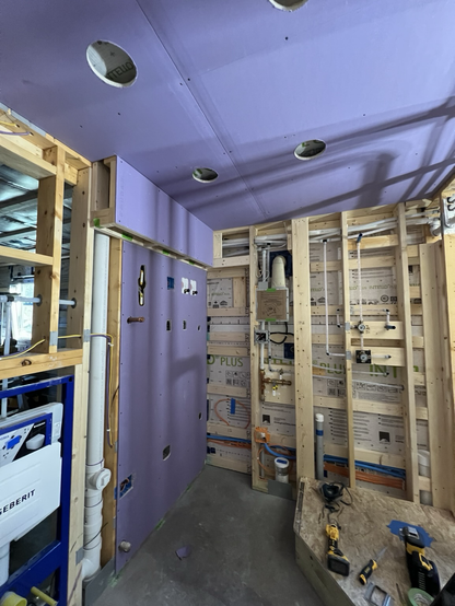 Bathroom drywall being installed, with several boards of purple mold resistant drywall already hung on the walls and ceiling.