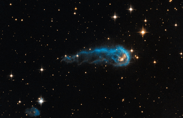 Hubble Space Telescope image showing IRAS 20324+4057, a bright blue, tadpole-shaped cloud of gas and dust in space surrounded by stars against a dark background.