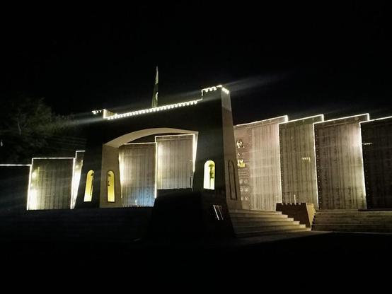 Night view of a war memorial with illuminated walls and a flag.