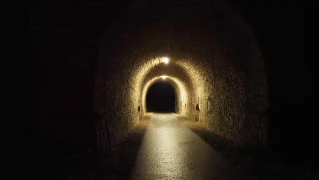 Beleuchteter Tunnel in dunkler Umgebung. Licht spiegelt sich auf nassem Asphalt