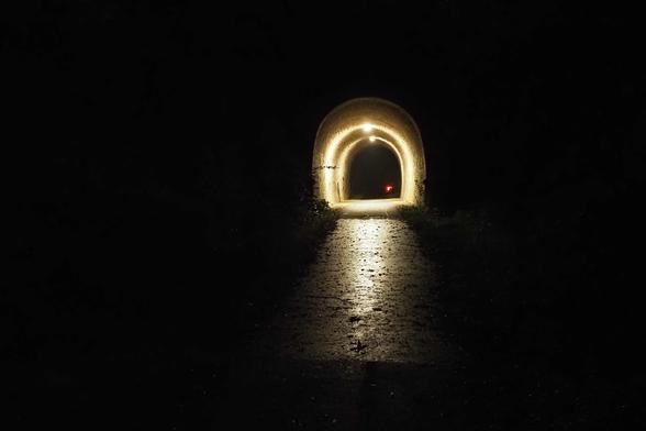 Beleuchteter Tunnel in dunkler Umgebung. Licht spiegelt sich auf nassem Asphalt