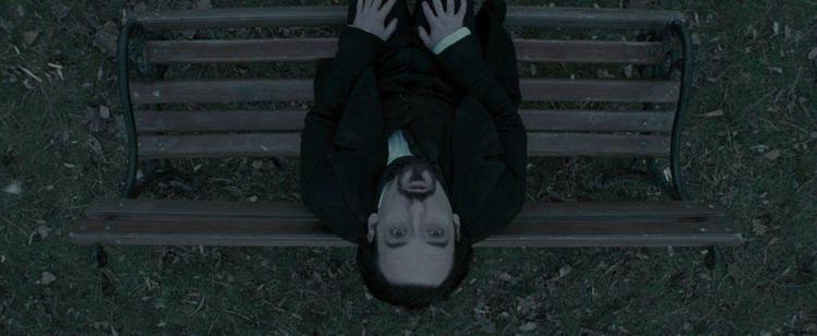 A dark-haired man tilts his head back on a bench, looking straight up into the sky