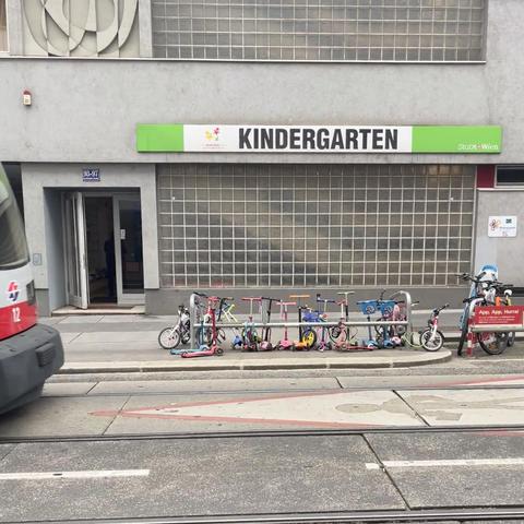 Die Fahrradbucht von der anderen Straßenseite fotografiert. Von dort sieht man nun auch das Kindergartenschild und Reihe Straßenbahn, die gerade Boot den Kindergarten vorbei und aus dem Bild fuhr
