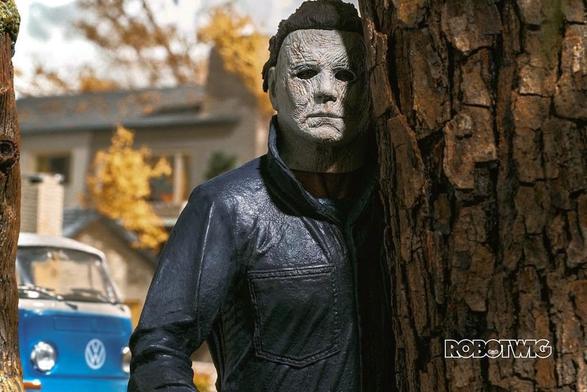 Michael Myers stands behind a tree in a suburban neighbourhood during the daytime