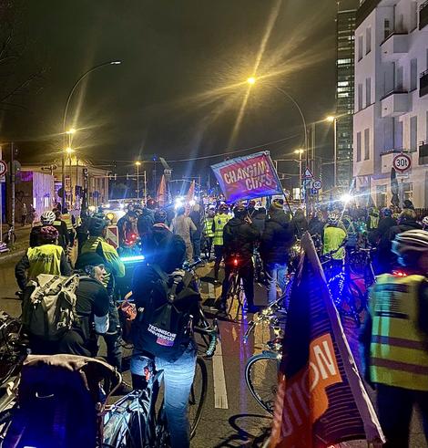 Auf dem Markgrafendamm findet eine Zwischenkundgebung der Respect Cyclists Fahrraddemo am 01.10.2025 statt, nahe der Kreuzung Richtung Elsenbrücke, in der Nähe des 16. Abschnitts der A100. Es ist dunkel, und die Stadtlichter beleuchten die Szene bunt.