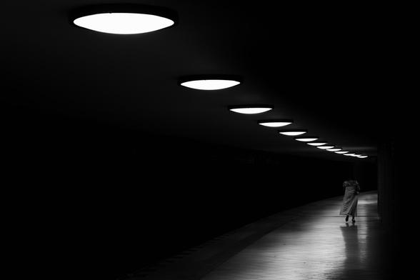A person walks down a subway station. Circular ceiling lights form a leading line.