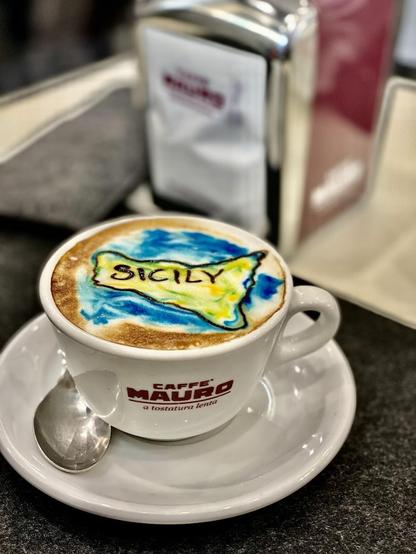 A cup of coffee with "SICILY" written on the foam in the shape of the island.