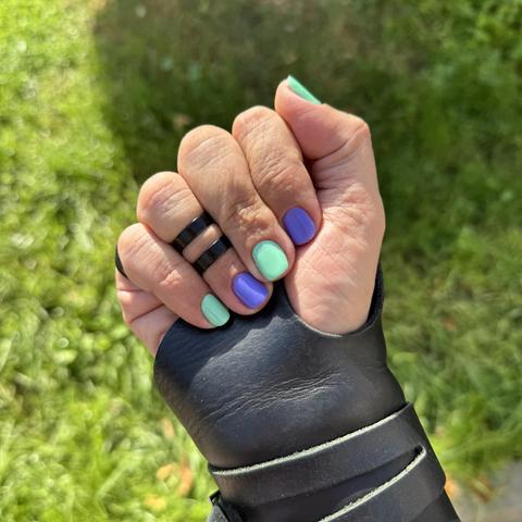 Mano derecha con muñequera de cuero cerrada mostrando las uñas alternando los colores aguamarina, lila, aguamarina, lila y aguamarina.