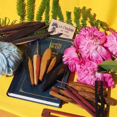 Des objets en bois posés sur un décor coloré. Il y a des crochets avec un manche en bois et des règles de lecture, des plioirs. Les bois sont pleins de couleurs différentes : pleins de marrons, du crème, du rose, du violet..