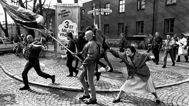 Danuta Danielsson hitting a Neo-Nazi with her handbag in Växjö, Sweden 1985; B&W photo of woman hitting a neo-Nazi from behind with her handbag