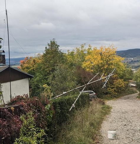 Zu sehen ist ein Antennen mast der umgelegt auf einer Hecke liegt. Es ist jeweils eine Yagi Antenn für 2M, 70cm und 23cm verbaut.