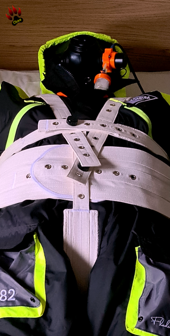 person wearing a yellow/grey/black floating suit, S10 gasmask and adidas sailing boots lying on a bed, tied in a segufix setup, closeup/bust view