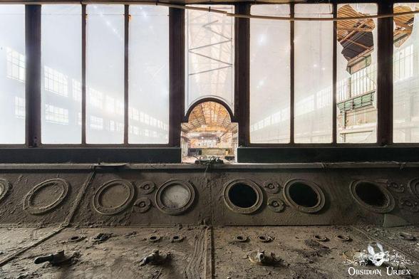 old control room panel. glass wall behind. a small window views over a large hall
