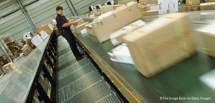 Ein Mann arbeitet an einem Laufband, auf dem mehrere Pakete unterschiedlicher Größe liegen.