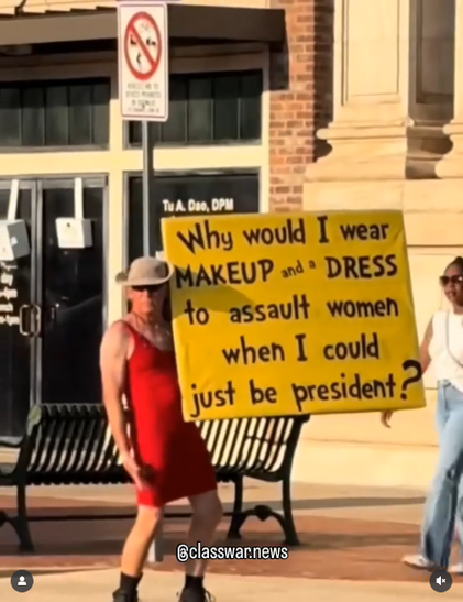 A cis man in a cowboy hat, sunglasses and tight red dress is standing on a street in Denton TX holding a yellow sign that says in black letters "Why would I wear makeup and a dress to assault women when I could just be president?"

It's a still of the video linked to.