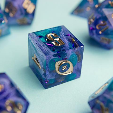 Zu sehen ist ein D6 in lila und türkisen Bloops die durch helle lila Schleier stechen.

Die Nummern sind in Gold geinked. Die Zahl 6 wurde durch mein Logo, ein Auge mit Stern, ausgetauscht.