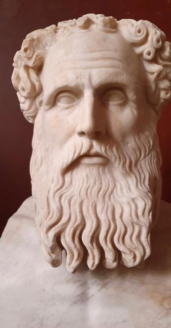 Scultura di un filosofo con barba e capelli mossi, rappresentata in marmo, evidenziando i dettagli del volto e dei capelli ricci.