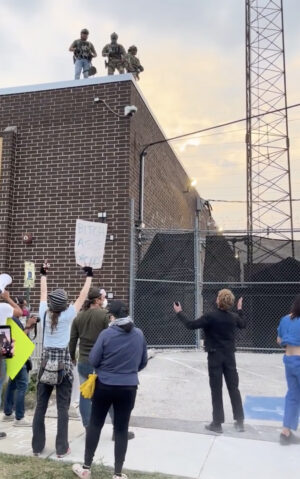 The Rev. David Black prays below masked agents on the rooftop of a U.S. Immigration and Customs Enforcement detention facility in Broadview, IL: