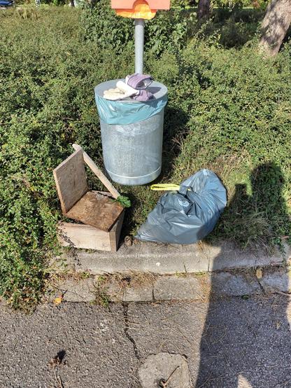 Ein Mülleimer, davor einige gesammelte Kleinteile und ein halber Sack mit aufgelesenem Müll. Auf dem Eimer liegen meine Handschuhe, im Hintergrund Gebüsch, vorne Asphalt, es ist sonnig.