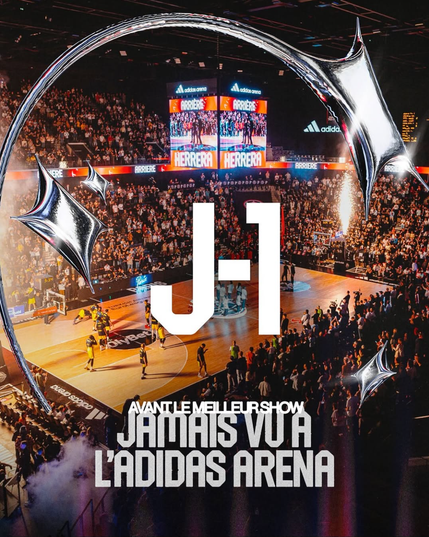 A vibrant basketball arena is filled with an excited crowd, featuring large screens and the text 'J-1' and 'Avant le meilleur show jamais vu à l'Adidas Arena.'