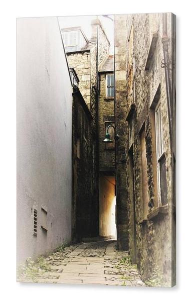 Colour portrait photo of an alley between old buildings.  Ahead a passage leads to the street and has a golden glow.  The image is shown printed upon a block canvas.