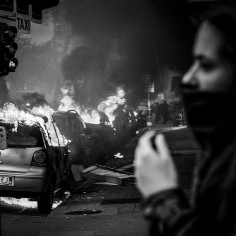 Des voitures qui brulent et une manifestante qui se cache le visage.