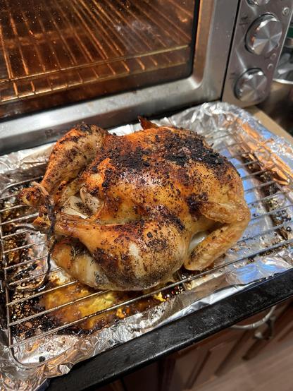 A roast chicken resting on a wire rack over a foil-lined tray.