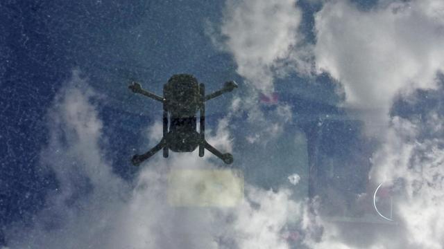 A flying drone and clouds in the sky are reflected in dirty moon roof glass.