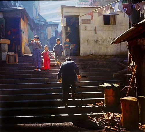 old man with cane headed up stairs, boy eating with chopsticks and red overall-wearing little brother head downstairs