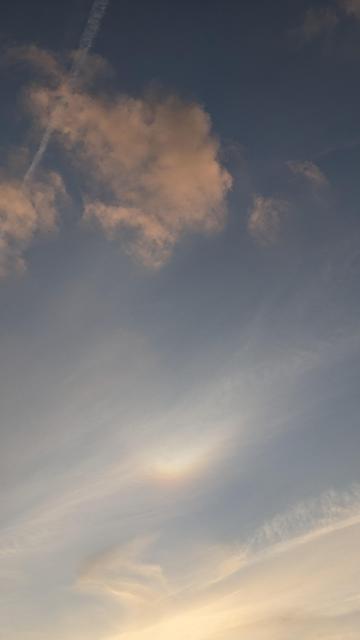 Morceau de ciel au soleil couchant, différentes strates de nuages diversement éclairés avec diverses teintes de roses. Au milieu un petit arc en ciel