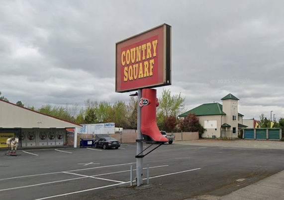 The sign for a western clothing company titled "COUNTRY SQUARE". It overlooks a parking lot. There is a giant red boot attached to the sign. The E has been modified into an F. "Country Squarf".