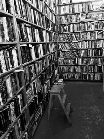 Black and white image of bookshelves filled with numerous books, with a small wooden step ladder in the foreground.