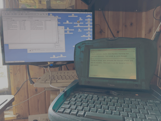 An green Apple Newton eMate in the foreground sat on a Quadra 610 with a monitor screen in the background