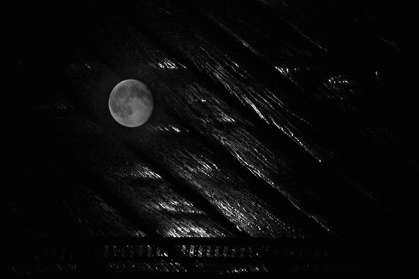 A roof at night with a really high humidity turned into water and is running down the roof. The moon is laying on the roof, and the moonlight is reflected in the moisture.