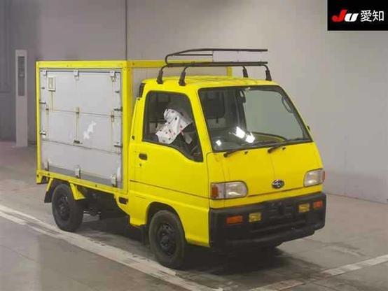 A bright yellow Subaru Sambar kei truck with a large grey box on the back. The box has folding sides to reveal a mobile kitchen contained within.