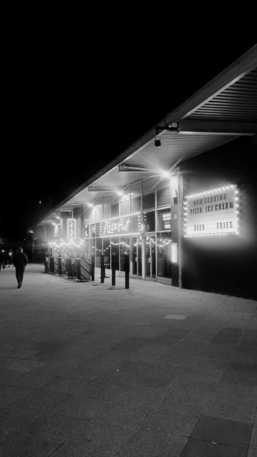 Brightly lit signs and strings of lights outside a Pizza Hut next to the cinema at night