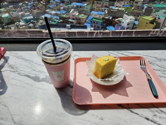 A coffee and cake on a pink tray are near a window.