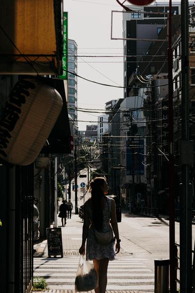 photo of a woman in a dress walking along a tightly packed street of Tokyo with a lot of power and telephone lines spanning across the street