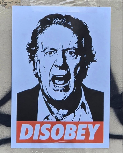 Poster su muro con la faccia di Enzo Iacchetti e sotto la scritta DISOBEY. 
[Obey Style]