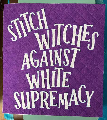 Small purple quilt with white letters reading “Stitch witches against white supremacy”