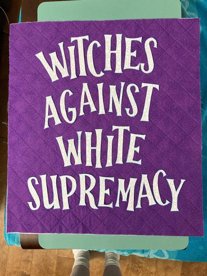 Small purple quilt with white letters that read “Witches against white supremacy”
