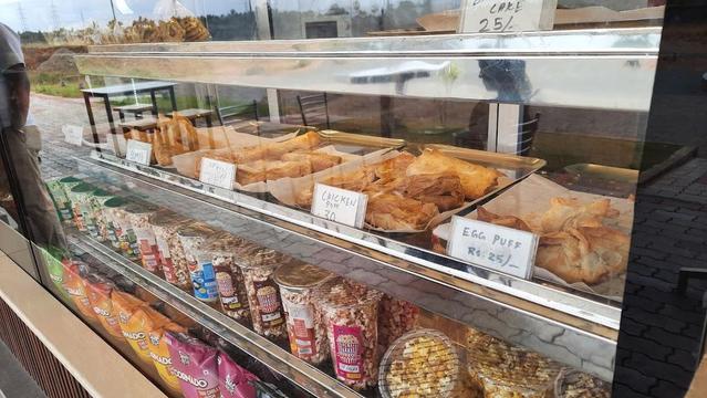 A bakery display case is filled with pastries like puffs and popcorn, with snacks on the bottom shelf.