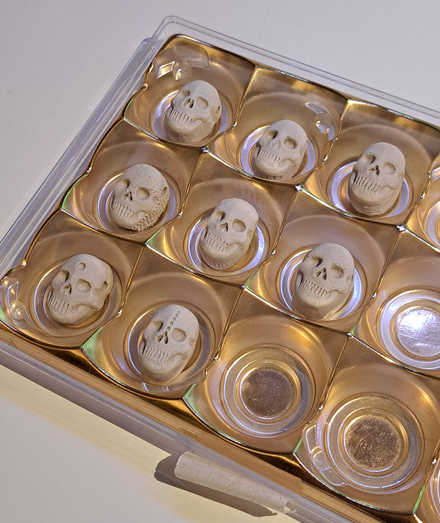 A plastic chocolate tray with greenware clay pendants in it. They are the shape of skulls.
