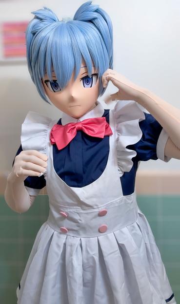 It’s a photo of a Nagisa Shiota kigurumi. He’s wearing a maid outfit. A mix of a dark blue blouse layered under a white frock with frilly shoulders and four pink buttons on the front. 

Nagisa looks a little embarrassed. He’s shaping a half a heart with his left hand, which is resting on his left cheek.