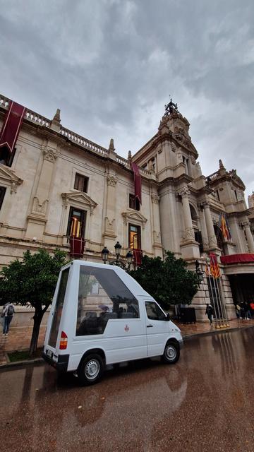 high roofed van with glazed area to transport a flag standing vertically. in front of Valencia City Hall