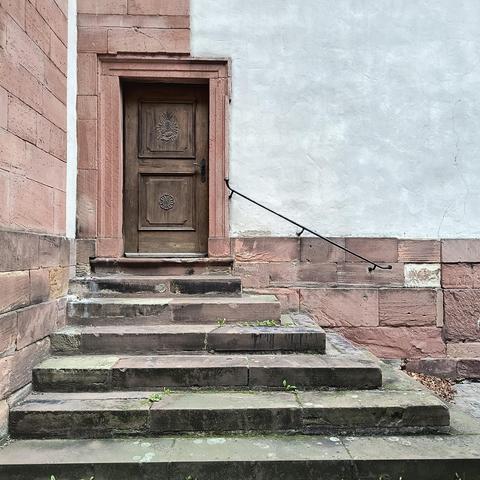 Deurtje bovenaan een trap in een hoekje aan de zijkant van de Muttergottespfarrkirche.
Rode zandsteen, bruinhouten deur, witgepleisterde muur.